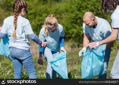 volunteering, charity, cleaning, people and ecology concept - group of happy volunteers with garbage bags cleaning area in park