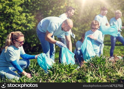 volunteering, charity, cleaning, people and ecology concept - group of happy volunteers with garbage bags cleaning area in park. volunteers with garbage bags cleaning park area. volunteers with garbage bags cleaning park area