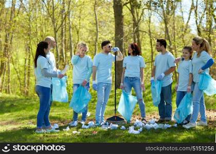 volunteering, charity, cleaning, people and ecology concept - group of happy volunteers with garbage bags and rake talking in park. group of volunteers with garbage bags in park