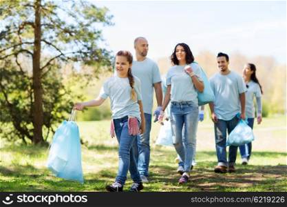 volunteering, charity, cleaning, people and ecology concept - group of happy volunteers with garbage bags walking in park