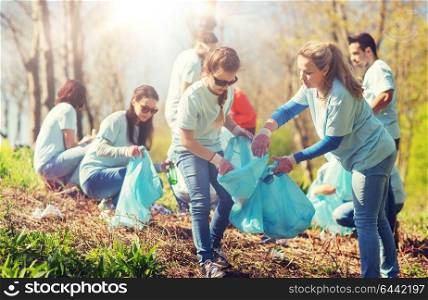volunteering, charity, cleaning, people and ecology concept - group of happy volunteers with garbage bags cleaning area in park. volunteers with garbage bags cleaning park area