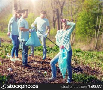volunteering, charity, cleaning, people and ecology concept - group of happy volunteers with garbage bags cleaning area in park. volunteers with garbage bags cleaning park area