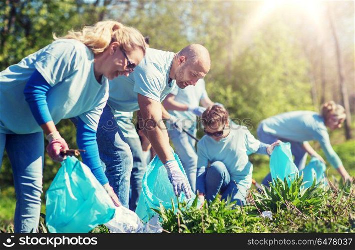 volunteering, charity, cleaning, people and ecology concept - group of happy volunteers with garbage bags cleaning area in park. volunteers with garbage bags cleaning park area. volunteers with garbage bags cleaning park area