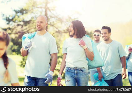 volunteering, charity, cleaning, people and ecology concept - group of happy volunteers with garbage bags walking in park. group of volunteers with garbage bags in park. group of volunteers with garbage bags in park