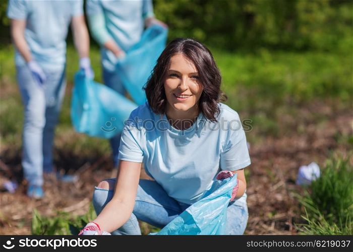 volunteering, charity, cleaning, people and ecology concept - happy woman and group of volunteers with garbage bags cleaning area in park