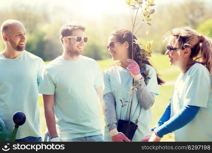 volunteering, charity, gardening, people and ecology concept - group of happy volunteers with tree seedlings and watering can in park. group of volunteers with tree seedling in park. group of volunteers with tree seedling in park