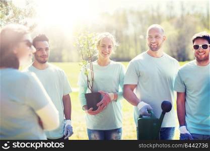 volunteering, charity, gardening, people and ecology concept - group of happy volunteers with tree seedlings and watering can in park. group of volunteers with tree seedling in park