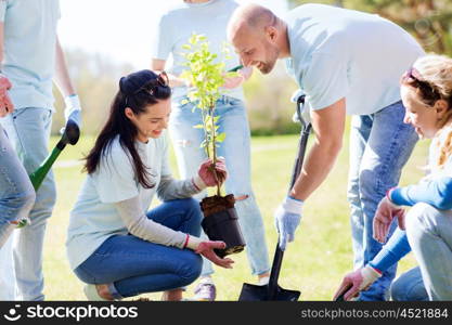 volunteering, charity, people and ecology concept - group of happy volunteers planting tree and digging hole with shovel in park