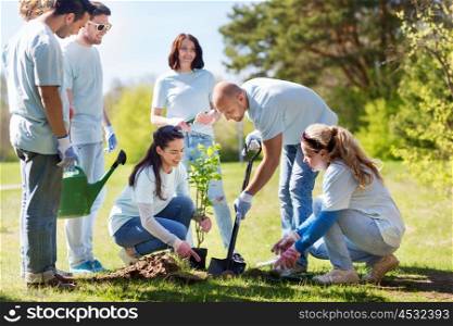 volunteering, charity, people and ecology concept - group of happy volunteers planting tree and digging hole with shovel in park