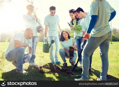 volunteering, charity, people and ecology concept - group of happy volunteers planting tree and digging hole with shovel in park. group of volunteers planting tree in park. group of volunteers planting tree in park
