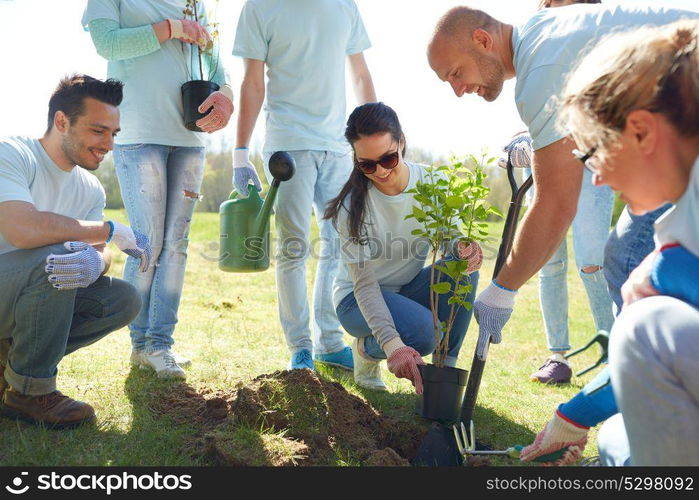 volunteering, charity, people and ecology concept - group of happy volunteers planting tree and digging hole with shovel in park. group of volunteers planting tree in park