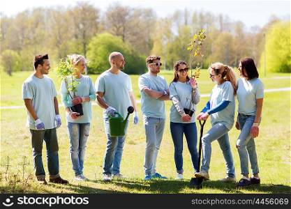 volunteering, charity, people and ecology concept - group of happy volunteers with tree seedlings and gardening tools in park