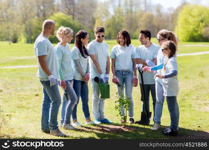 volunteering, charity, people and ecology concept - group of happy volunteers with watering can and shovel planting tree in park
