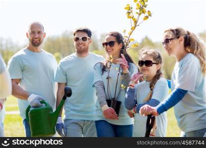volunteering, charity, people and ecology concept - group of happy volunteers with tree seedlings and gardening tools in park
