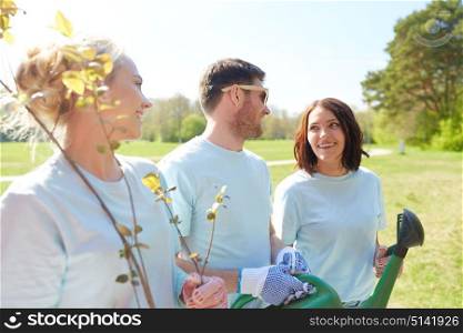volunteering, charity, people and ecology concept - group of happy volunteers with tree seedlings and watering can talking in park. group of volunteers with tree seedlings in park