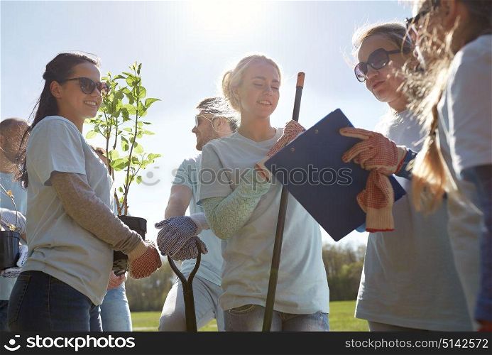 volunteering, charity, people and ecology concept - group of happy volunteers with tree seedlings and clipboard in park. group of volunteers with tree seedlings in park