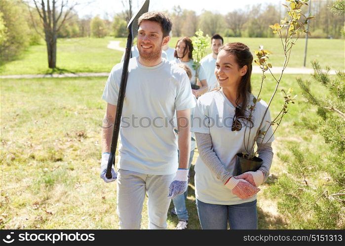 volunteering, charity, people and ecology concept - group of happy volunteers with tree seedlings and shovel in park. group of volunteers with trees and rake in park