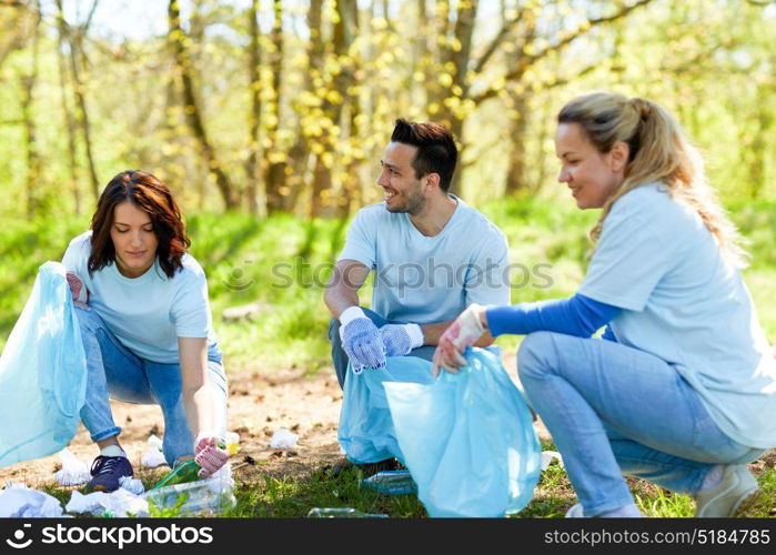 volunteering, charity, people and ecology concept - group of happy volunteers with garbage bags cleaning area in park. volunteers with garbage bags cleaning park area