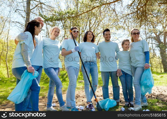 volunteering, charity, people and ecology concept - group of happy volunteers with garbage bags and rake cleaning area in park. volunteers with garbage bags cleaning park area