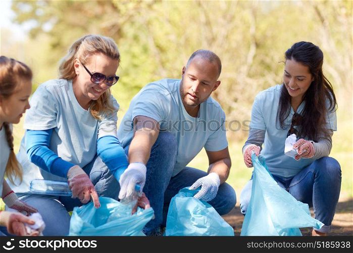 volunteering, charity, people and ecology concept - group of happy volunteers with garbage bags cleaning area in park. volunteers with garbage bags cleaning park area