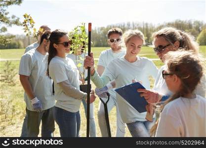 volunteering, charity, people and ecology concept - group of happy volunteers with tree seedlings and clipboard in park. group of volunteers with tree seedlings in park