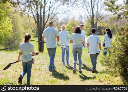 volunteering, charity, people and ecology concept - group of happy volunteers with tree seedlings and garden tools walking in park. happy volunteers with seedlings and garden tools