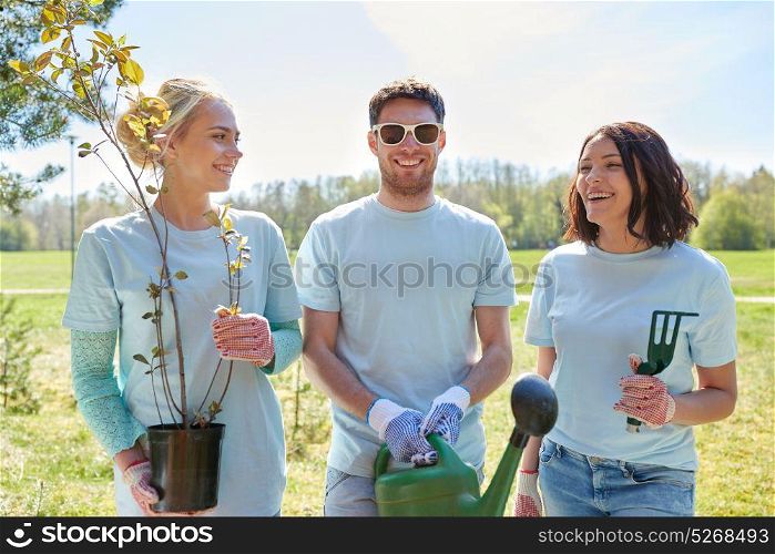 volunteering, charity, people and ecology concept - group of happy volunteers with tree seedlings and watering can in park. group of volunteers with tree seedlings in park