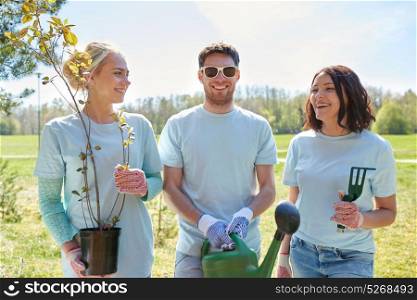 volunteering, charity, people and ecology concept - group of happy volunteers with tree seedlings and watering can in park. group of volunteers with tree seedlings in park