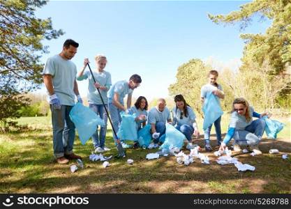 volunteering, charity, people and ecology concept - group of happy volunteers with garbage bags and rake cleaning area in park. volunteers with garbage bags cleaning park area