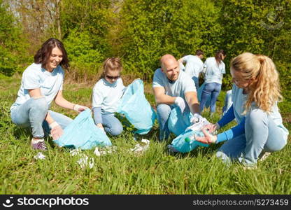 volunteering, charity, people and ecology concept - group of happy volunteers with garbage bags cleaning area in park. volunteers with garbage bags cleaning park area