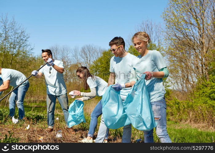 volunteering, charity, people and ecology concept - group of happy volunteers with garbage bags cleaning area in park. volunteers with garbage bags cleaning park area