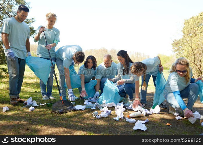 volunteering, charity, people and ecology concept - group of happy volunteers with garbage bags and rake cleaning area in park. volunteers with garbage bags cleaning park area