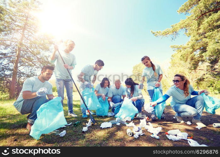 volunteering, charity, people and ecology concept - group of happy volunteers with garbage bags and rake cleaning area in park. volunteers with garbage bags cleaning park area. volunteers with garbage bags cleaning park area