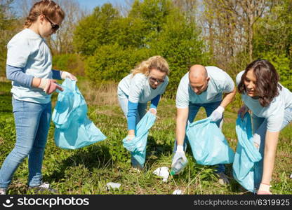 volunteering, charity, people and ecology concept - group of happy volunteers with garbage bags cleaning area in park. volunteers with garbage bags cleaning park area