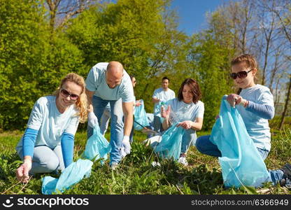 volunteering, charity, people and ecology concept - group of happy volunteers with garbage bags cleaning area in park. volunteers with garbage bags cleaning park area