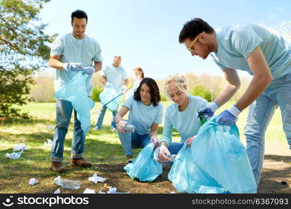 volunteering, charity, people and ecology concept - group of happy volunteers with garbage bags cleaning area in park. volunteers with garbage bags cleaning park area