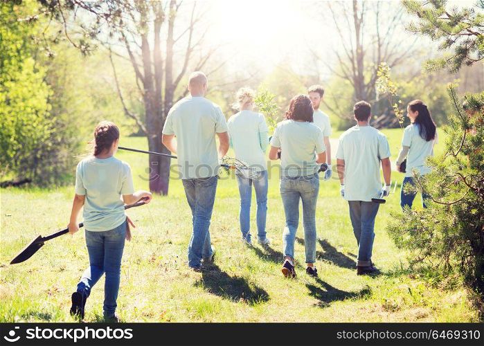 volunteering, charity, people and ecology concept - group of happy volunteers with tree seedlings and garden tools walking in park. happy volunteers with seedlings and garden tools