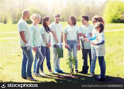 volunteering, charity, people and ecology concept - group of happy volunteers with watering can and shovel planting tree in park. group of volunteers planting tree in park