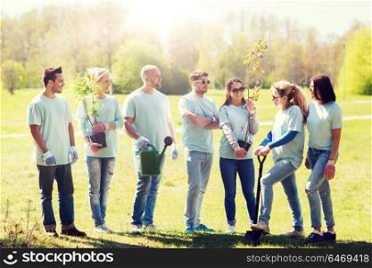 volunteering, charity, people and ecology concept - group of happy volunteers with tree seedlings and gardening tools in park. group of volunteers with trees and rake in park