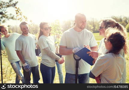 volunteering, charity, people and ecology concept - group of happy volunteers with tree seedlings and clipboard talking in park. group of volunteers with tree seedlings in park. group of volunteers with tree seedlings in park