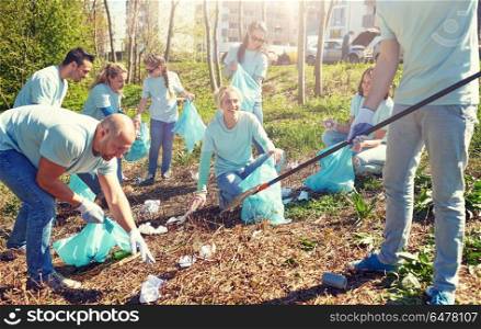 volunteering, charity, people and ecology concept - group of happy volunteers with garbage bags and rake cleaning area in park. volunteers with garbage bags cleaning park area. volunteers with garbage bags cleaning park area