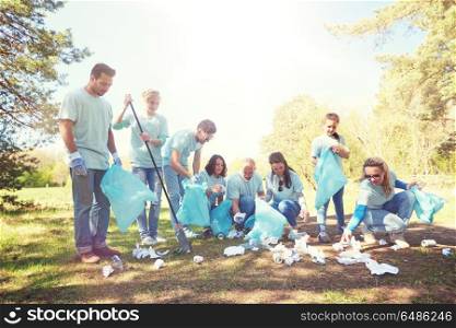 volunteering, charity, people and ecology concept - group of happy volunteers with garbage bags and rake cleaning area in park. volunteers with garbage bags cleaning park area. volunteers with garbage bags cleaning park area