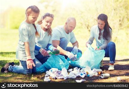 volunteering, charity, people and ecology concept - group of happy volunteers with garbage bags cleaning area in park. volunteers with garbage bags cleaning park area. volunteers with garbage bags cleaning park area