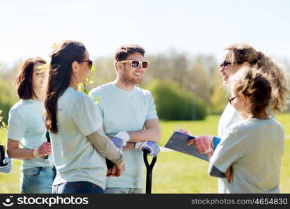 volunteering, charity, people and ecology concept - group of volunteers with clipboard planting trees in park. group of volunteers planting trees in park