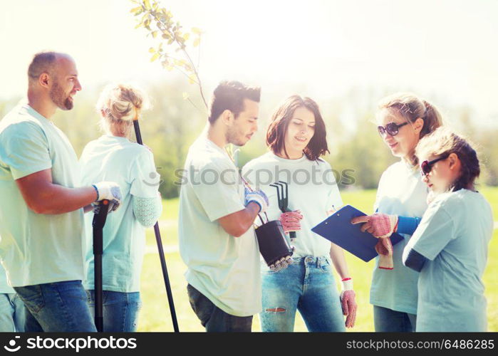 volunteering, charity, people and ecology concept - group of volunteers with clipboard planting trees in park. group of volunteers planting trees in park. group of volunteers planting trees in park