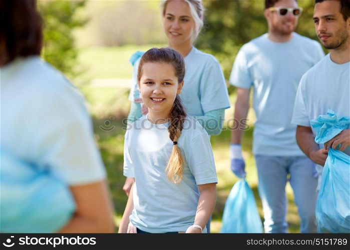 volunteering, charity, people and ecology concept - happy girl with group of volunteers cleaning garbage outdoors. volunteers with garbage bags outdoors