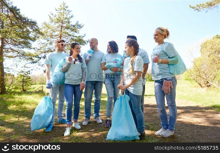 volunteering, charity, people and ecology concept - happy young volunteers with garbage bags walking outdoors. volunteers with garbage bags walking outdoors