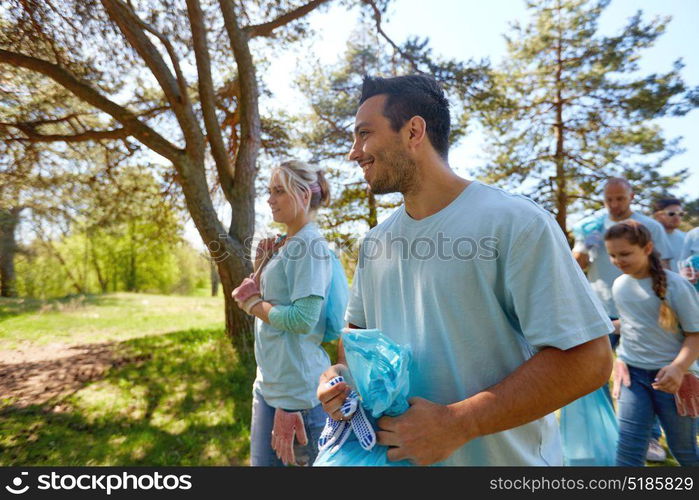 volunteering, charity, people and ecology concept - happy young volunteers with garbage bags walking outdoors. volunteers with garbage bags walking outdoors