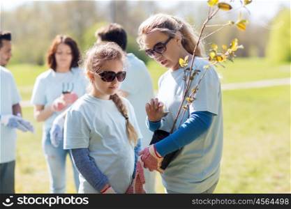 volunteering, charity, people, family and ecology concept - mother and daughter volunteer with tree seedling in park