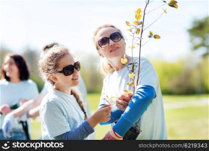 volunteering, charity, people, family and ecology concept - mother and daughter volunteer with tree seedling in park